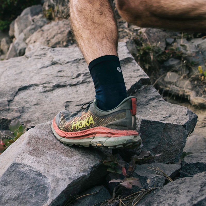 close-up of a man's leg wearing trail running shoes, stepping on a rocky trail