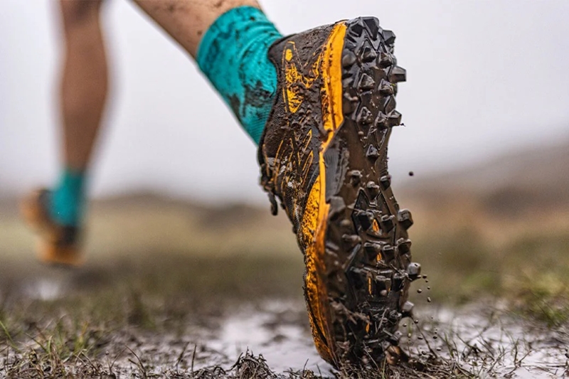 close up of a mans leg wearing trail running shoes on a muddy trail