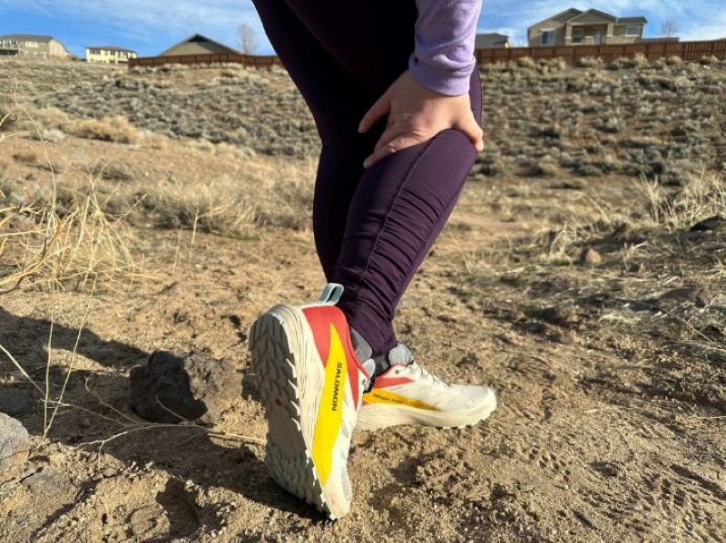 close up of a womans leg wearing salomon trail running shoes on a sandy trail